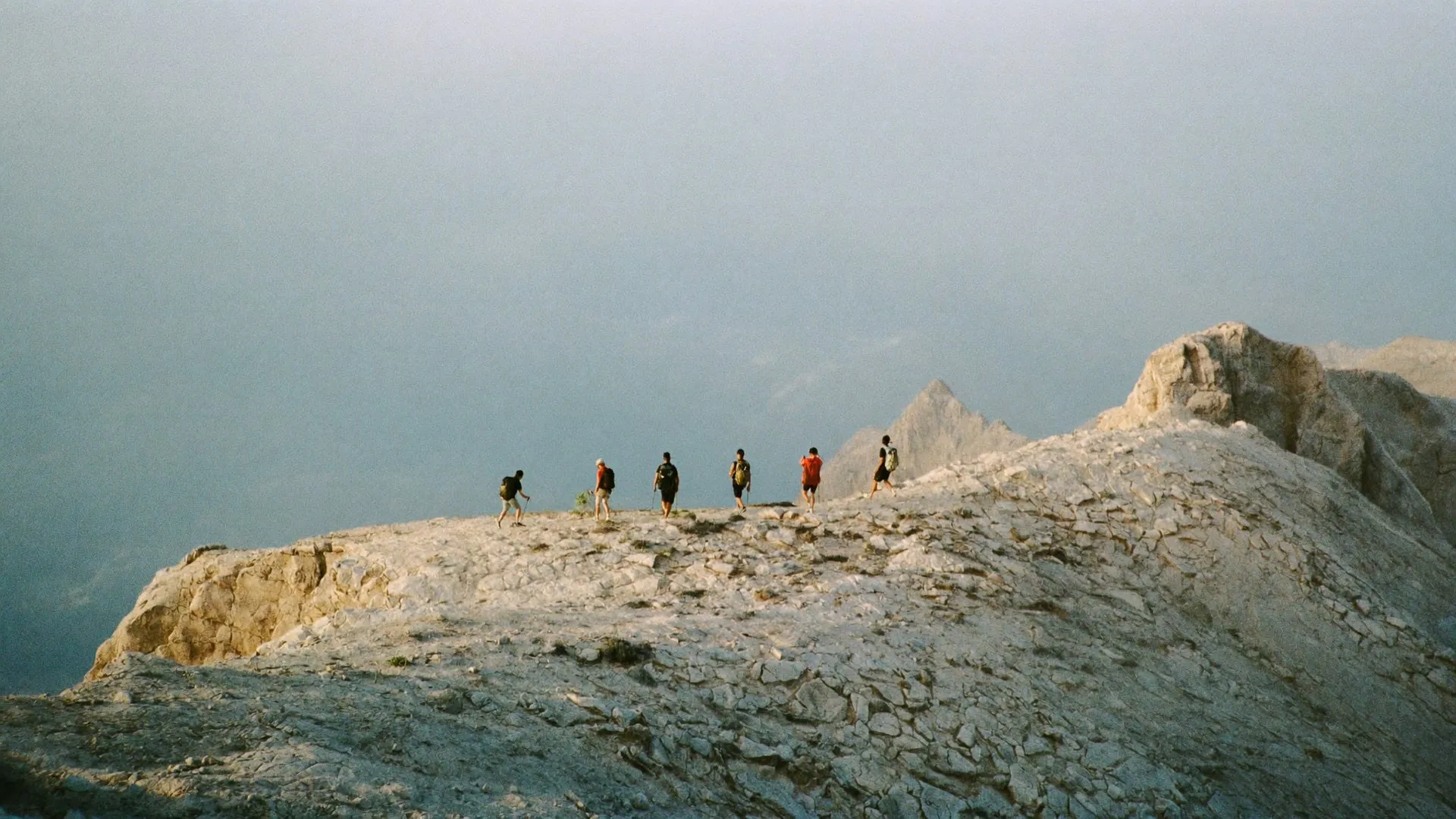 Grupo de senderistas caminando en fila por una cresta de montaña al amanecer